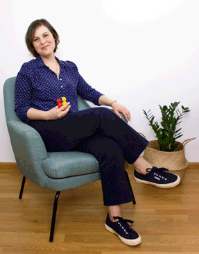 Foto Therapeutin Naima Cosa in ihrem Praxisraum, sitzend auf einem mintgrünen Stuhl, einladend lächelnd, im Hintergrund eine grüne Zimmerpflanze.